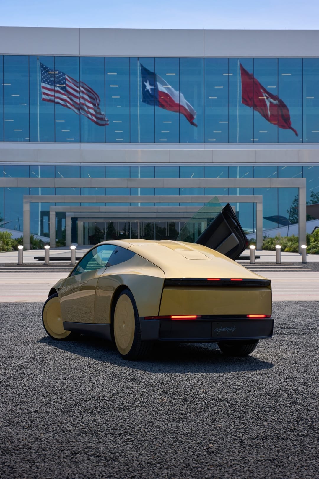 Gold Cybercab with doors open in front of a Tesla building with flags