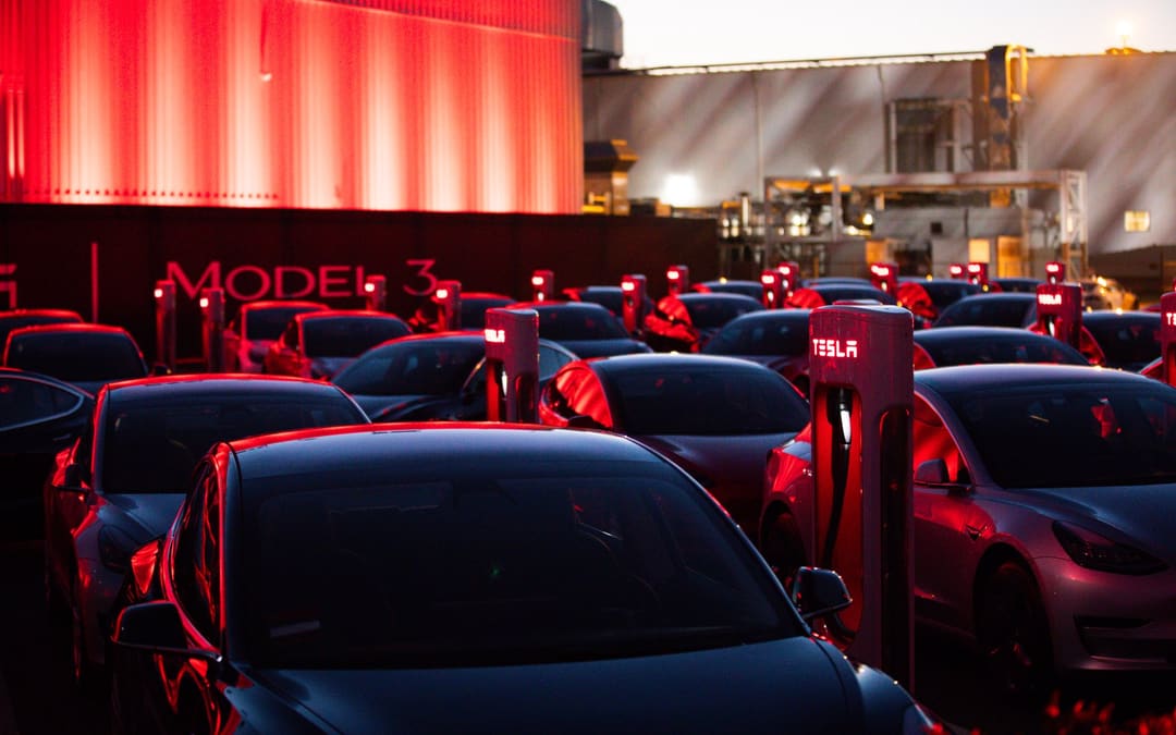 Rows of Model 3 cars at a red-lit Tesla Supercharger, from Tesla’s “10 years of Model 3” post