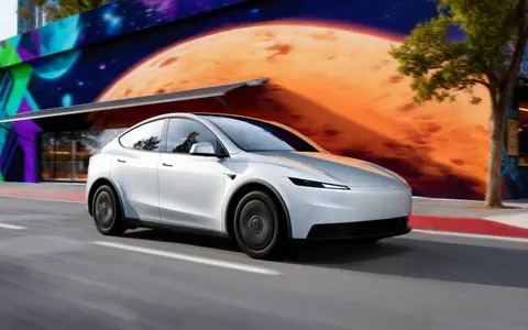 White Tesla Model Y driving past a colorful mural (Tesla photo)