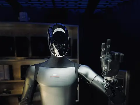 Optimus humanoid robot in a dimly lit room, raising its right hand in a wave